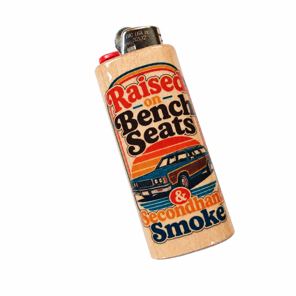 A novelty lighter with a light wood grain finish, featuring a retro-style label that reads 'Raised on Bench Seats & Secondhand Smoke' with an illustration of a vintage station wagon against a sunset, on a plain white background.
